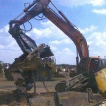 A DARK METALS excavator equipped with steel shear destroys redundant earthmoving machinery.